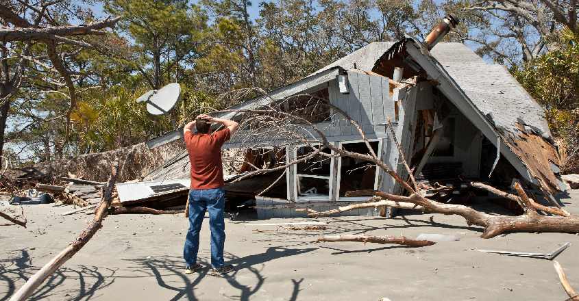 Muž stojící u stromem zničeného domu s pojištěním nemovitosti.