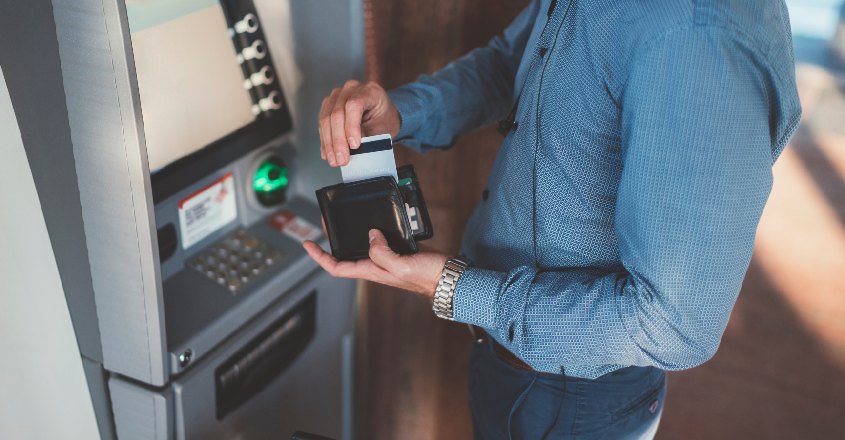Muž stojící u bankomatu vytahuje z peněženky kreditní kartu.