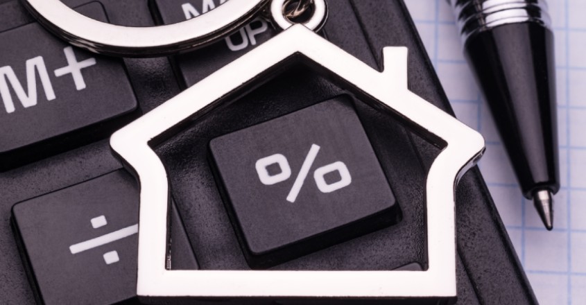 Přívěsek ve tvaru domu ležící na klávese se značkou %.