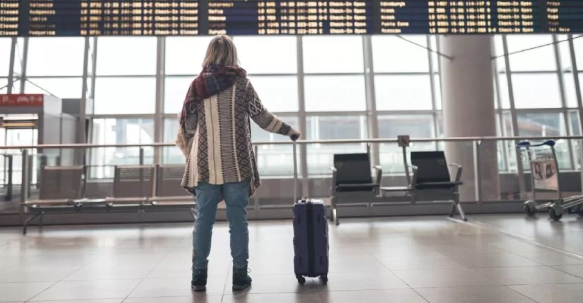Žena stojící před letovou tabulí a čekají na odlet.