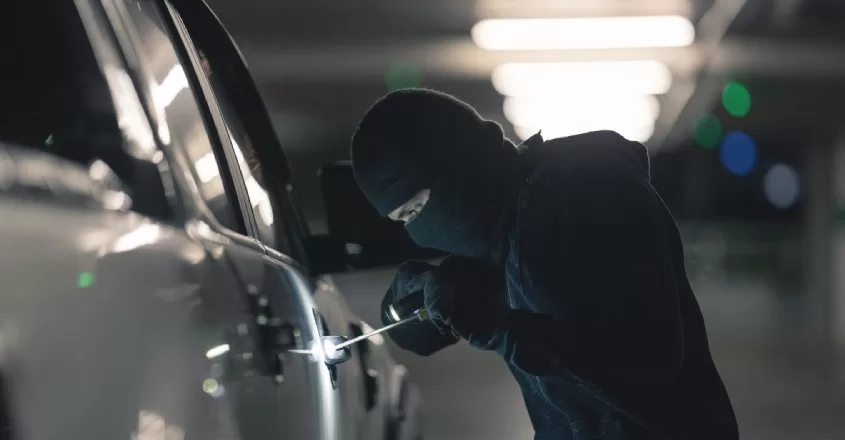 Maskovaný zloděj se v podzemních garáží snaží vloupat do zamčeného auta.