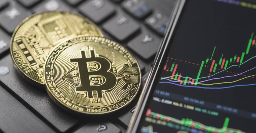 Mince se znakem Bitcoin položené na klávesnici vedle telefonu