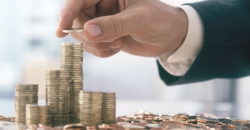 Rok 2025 pravděpodobně přinese další pokles úrokových sazeb, což může snížit atraktivitu spořicích účtů jako hlavního nástroje pro zhodnocení úspor. Ruka dávající minci na hromadu mincí
